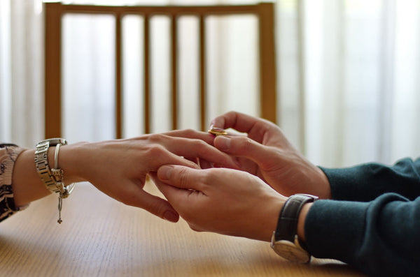 Just Gold Jewellery - Closeup of man placing engagement ring on womens hand