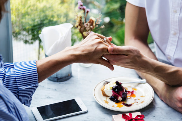 Man and women holding hands on a table with a nice dish and mobile phone on table