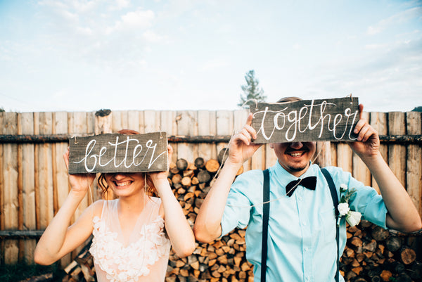 A women holding a sign in front of face with the word 'better' next to a man holding a sign in front of face with the word 'together'