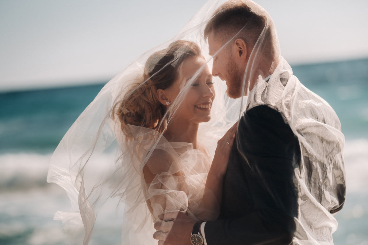 Happy bride and groom under the brides veil by the sea